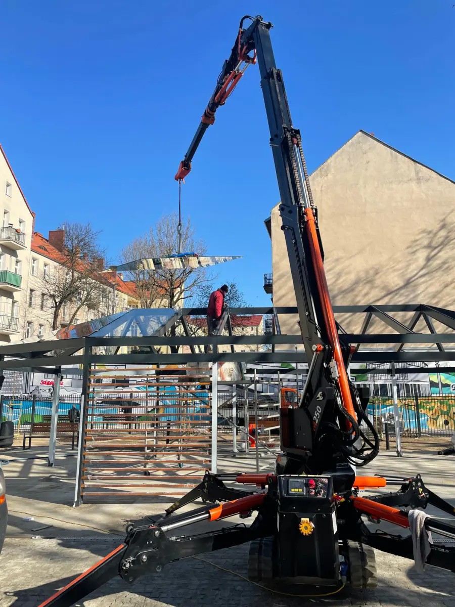 Mini żuraw JK Lift układa taflę szkła na stalowej konstrukcji zadaszenia pawilonu w centrum Gorzowa