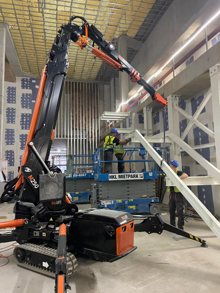 Mini żuraw BG Lift M250 ustawia stalowy bieg schodów wewnątrz budowanego obiektu w Niemczech