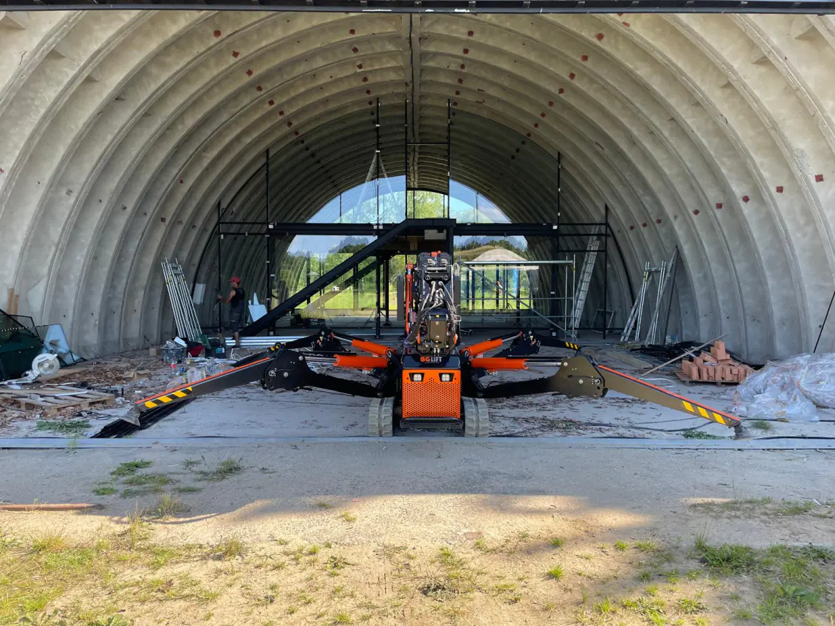 Mini żuraw JK Lift wjeżdża do łukowej hali w Niemczech, w której powstaje przeszklona zabudowa