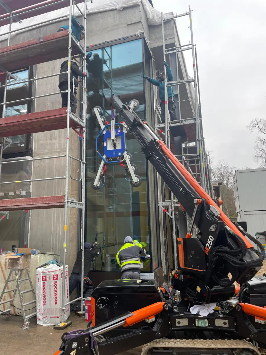 Ekipa monterów z mini żurawiem JK Lift szkli narożnik budynku w rusztowaniu w Niemczech